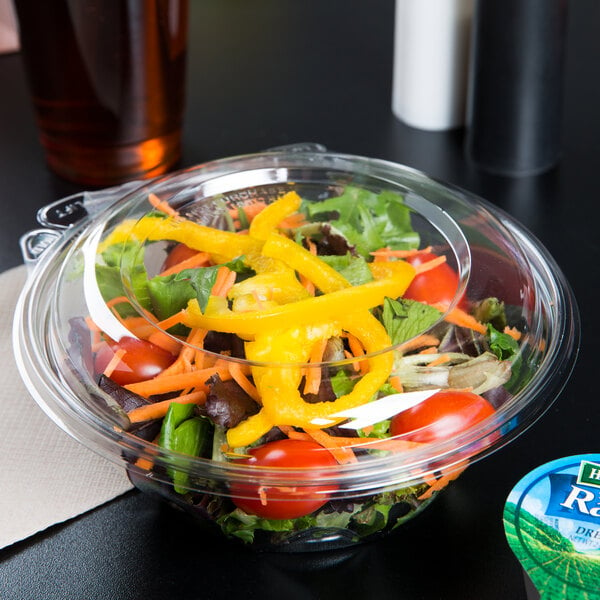 A salad in a Dart plastic bowl with a drink on a table.
