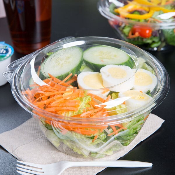 A Dart plastic bowl filled with salad with a fork and knife on top.