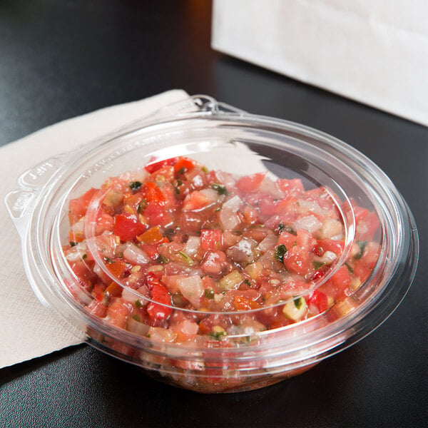 A Dart plastic container of salsa on a table.