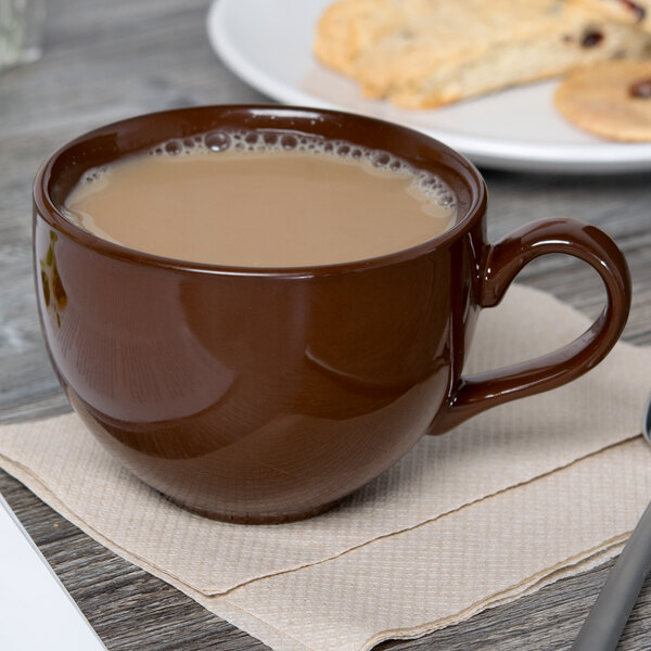 A Tuxton mahogany cappuccino cup filled with a brown drink on a napkin next to a plate of cookies.