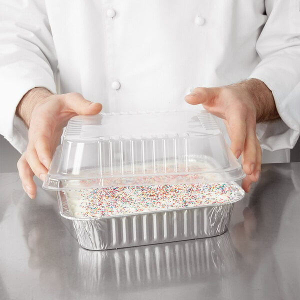 A person holding a Durable Packaging square foil cake pan with white frosting and sprinkles.
