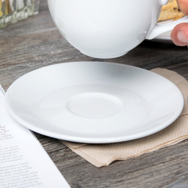 A hand pouring coffee into a white Tuxton porcelain saucer.