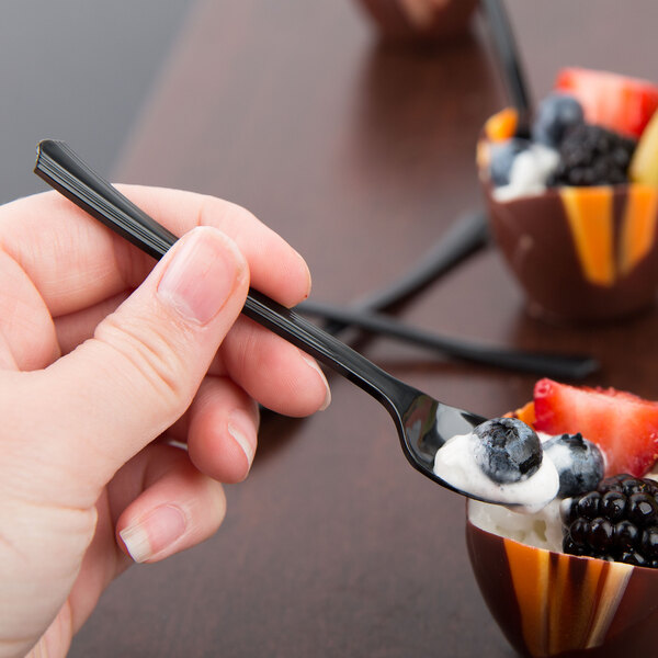 A hand holding a WNA Comet black tasting spoon with fruit in a bowl.