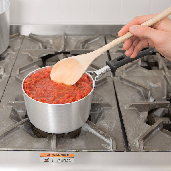 A person stirring red sauce in a Vollrath Wear-Ever sauce pan on a stove.