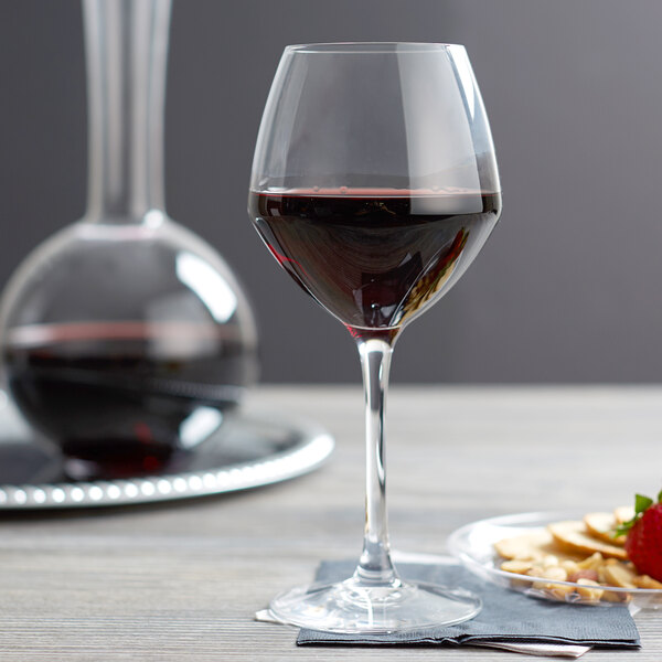 A Chef & Sommelier Cabernet wine glass filled with red wine next to a plate of strawberries.
