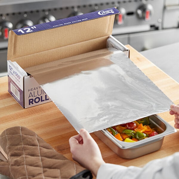A person using Choice heavy-duty aluminum foil to cover a tray of food.