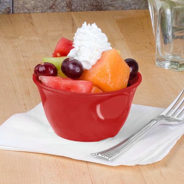 A red Thunder Group melamine bouillon bowl filled with fruit and whipped cream with a fork.
