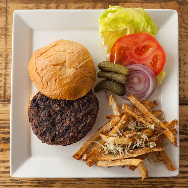 A 10 Strawberry Street Whittier Elite square white porcelain plate with a burger and fries on a wood table.