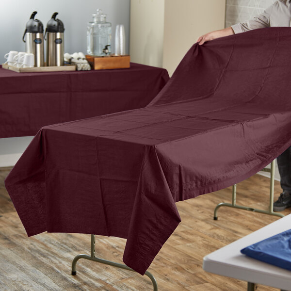A person holding a table with a burgundy Hoffmaster table cover.