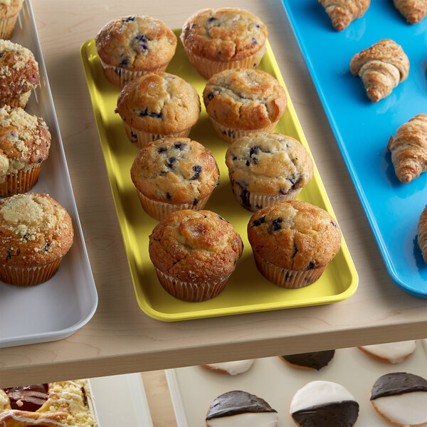 A yellow Cambro market tray with muffins and croissants on a bakery shelf.