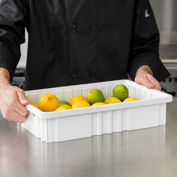 A person holding a Metro white divider tote box filled with lemons and limes.