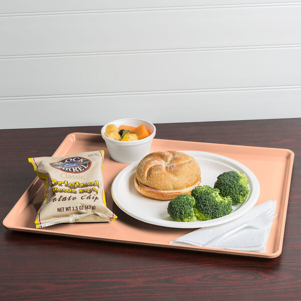 A Cambro dark peach dietary tray with a sandwich, broccoli, and potato chips.