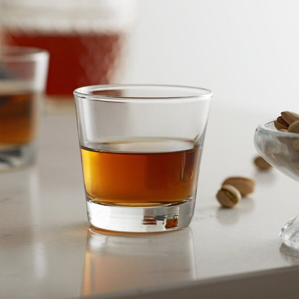 A Libbey customizable rocks glass filled with brown liquid next to pistachios.