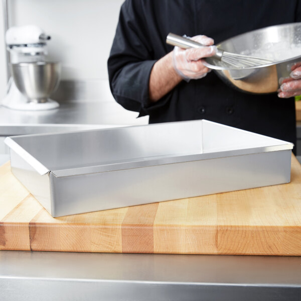 A chef mixing ingredients in a Vollrath Wear-Ever aluminum cake pan.