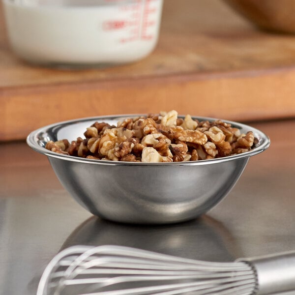 A white bowl filled with walnuts and a whisk on a table.