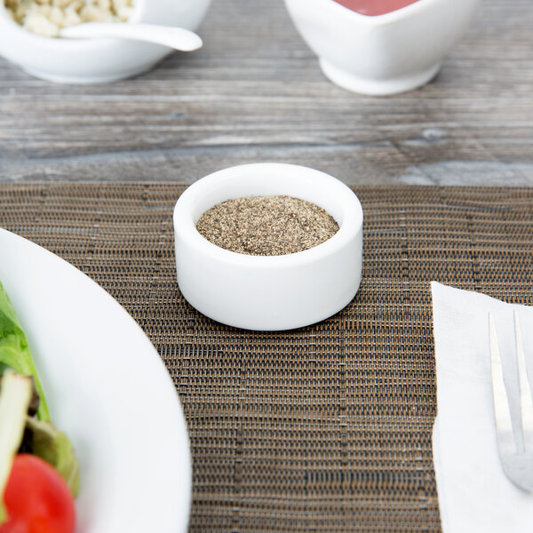 A white American Metalcraft porcelain bowl of pepper next to a plate of salad.