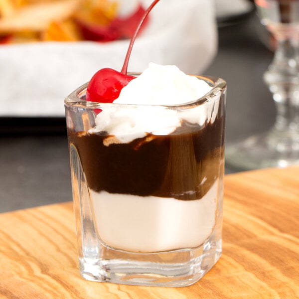 A Libbey square shot glass filled with chocolate pudding and topped with whipped cream and a cherry.