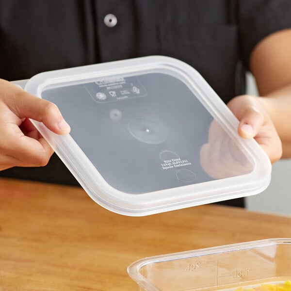 A person holding a Cambro translucent square polypropylene food storage container.