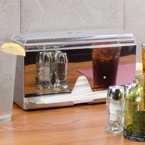 A stainless steel Vollrath Straw Boss dispenser on a counter next to a glass of brown liquid with ice.