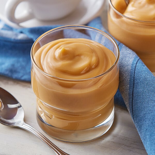 A glass of Cafe Classics butterscotch pudding with a spoon and a blue napkin.