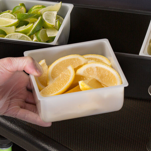 A hand holding a Tablecraft white condiment dispenser filled with lemon wedges.