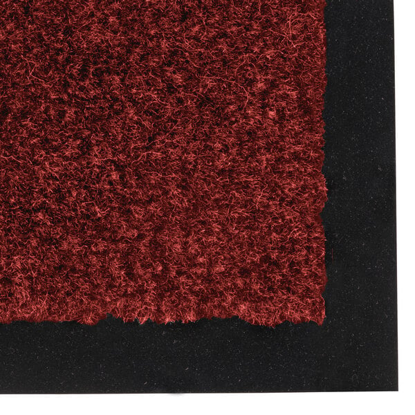 A close up of a crimson Notrax carpet entrance floor mat with black trim.