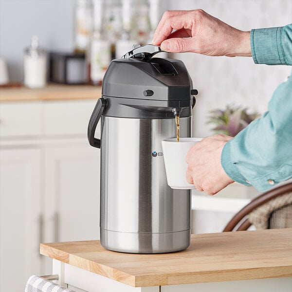 A person using a Bunn stainless steel coffee airpot to pour coffee.