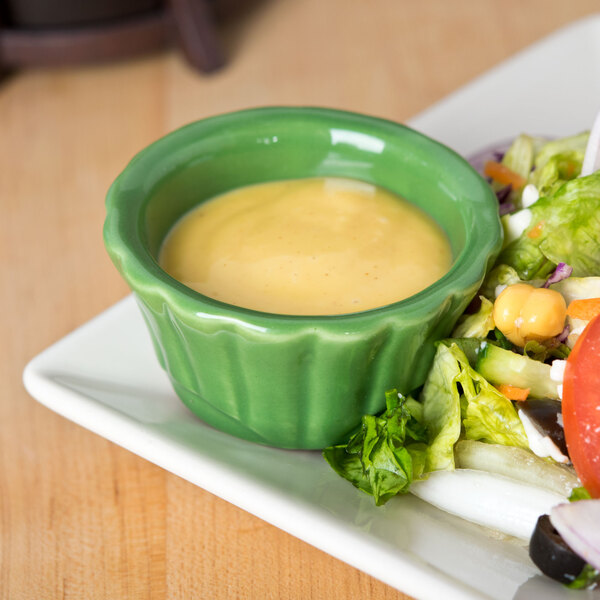 A plate of salad with a small green bowl of yellow sauce.