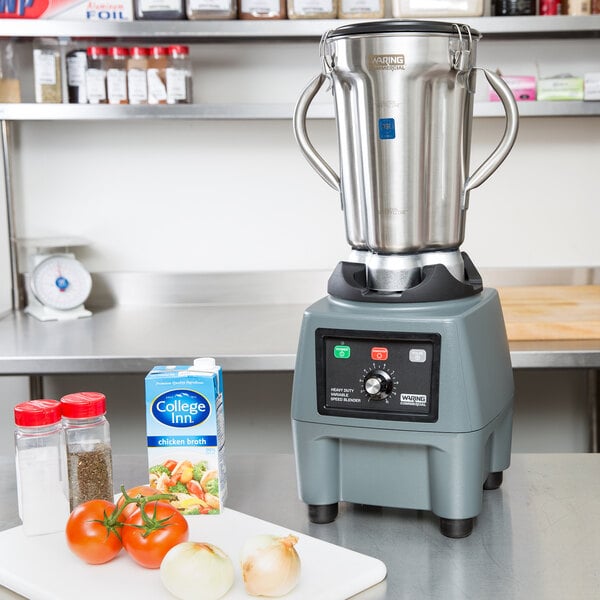 A Waring food blender on a counter with vegetables, spices, and a tomato.