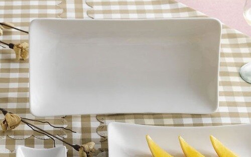 A white rectangular CAC porcelain platter on a table with a knife and a banana.