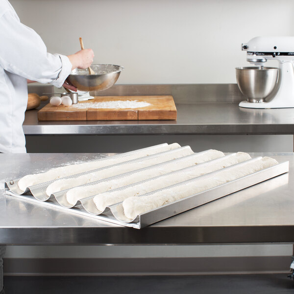 A person in a white coat mixing dough in a Chicago Metallic baguette pan.