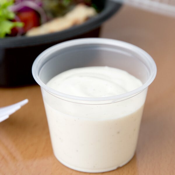 A Dart clear plastic souffle cup filled with white sauce.