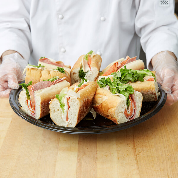 A person holding a plate of sandwiches with lettuce, ham, and meat.
