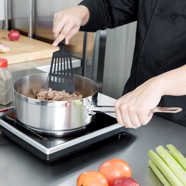 A person cooking food in a Vollrath stainless steel saucier pan.