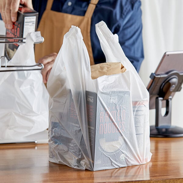 A person holding a white plastic Choice T-Shirt Bag full of groceries.
