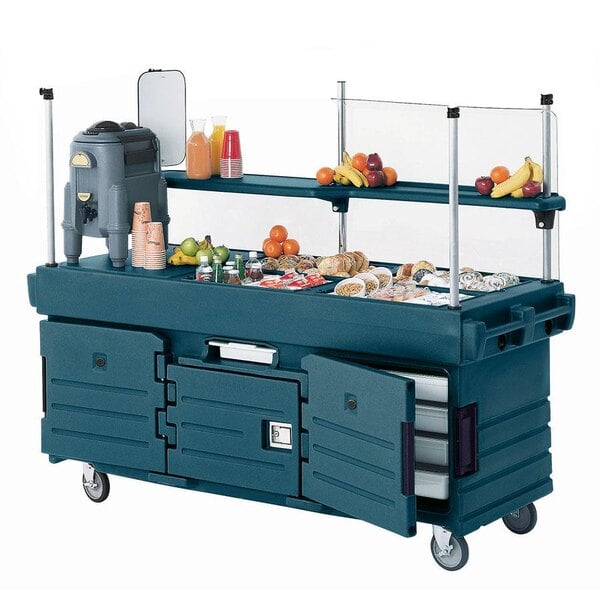 A granite green Cambro CamKiosk vending cart with pan wells on a table in an outdoor catering setup.