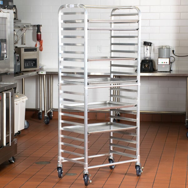 A Regency stainless steel side load sheet pan rack with wheels holding four trays in a kitchen.