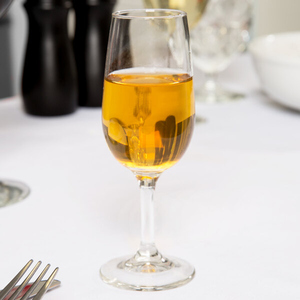 A Libbey Bristol Valley sherry glass filled with yellow liquid on a table with silverware.