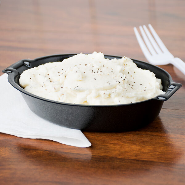 A black Dart foam oval casserole dish filled with mashed potatoes and a fork on a plate.