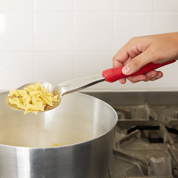 A person using a Vollrath Jacob's Pride heavy-duty perforated basting spoon with a red Ergo grip to serve pasta.