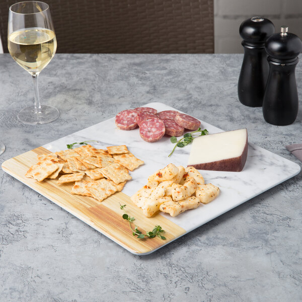 An Elite Global Solutions Sierra Carrara marble serving board with food and a glass of white wine on a table.