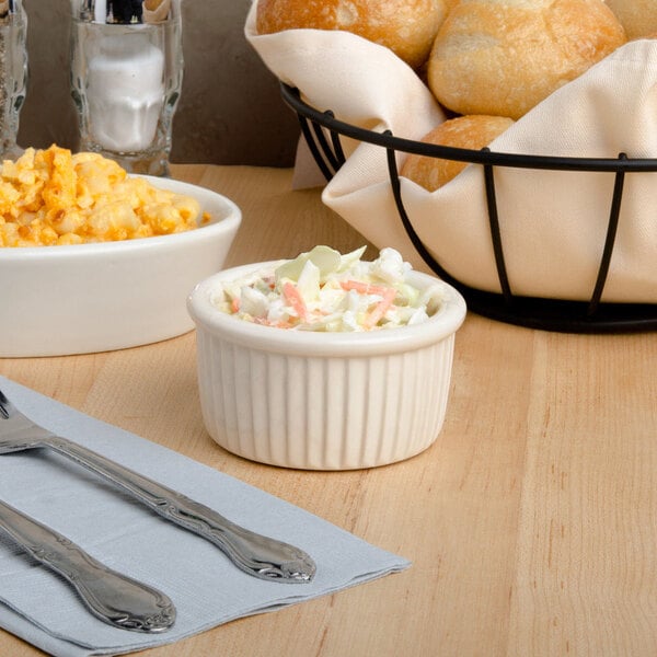 A white Tuxton fluted ramekin filled with macaroni and cheese on a table with coleslaw and bread.