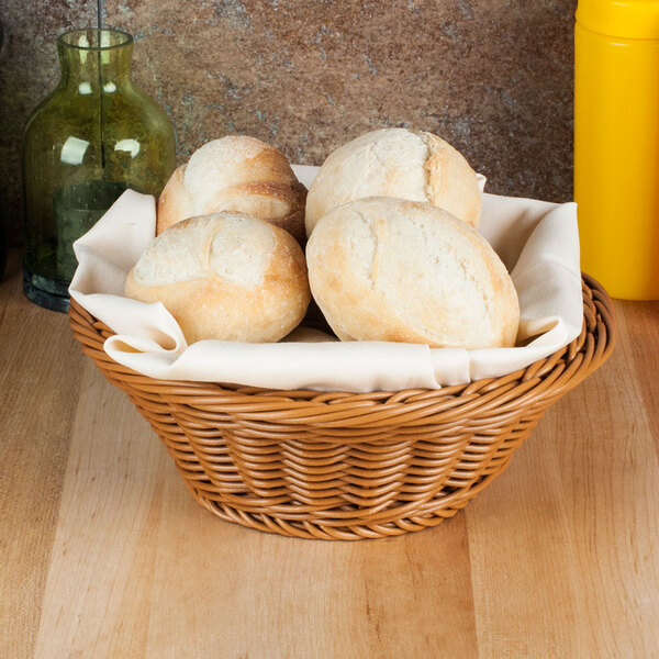 A round honey polyweave bread basket on a table with bread inside.
