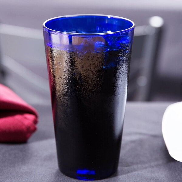 A close up of a Libbey cobalt blue cooler glass filled with a drink on a table with a white circle and black border.