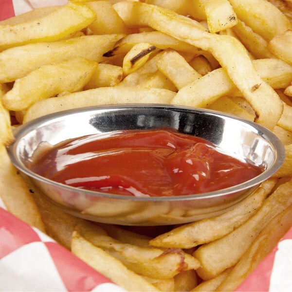 A bowl of ketchup in a stainless steel sauce cup with french fries.