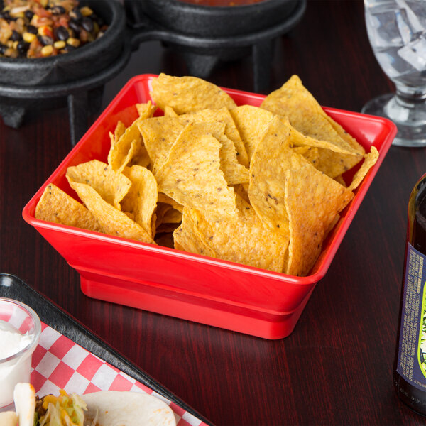 A red HS Inc. polyethylene square basket filled with chips on a table in a Mexican restaurant.