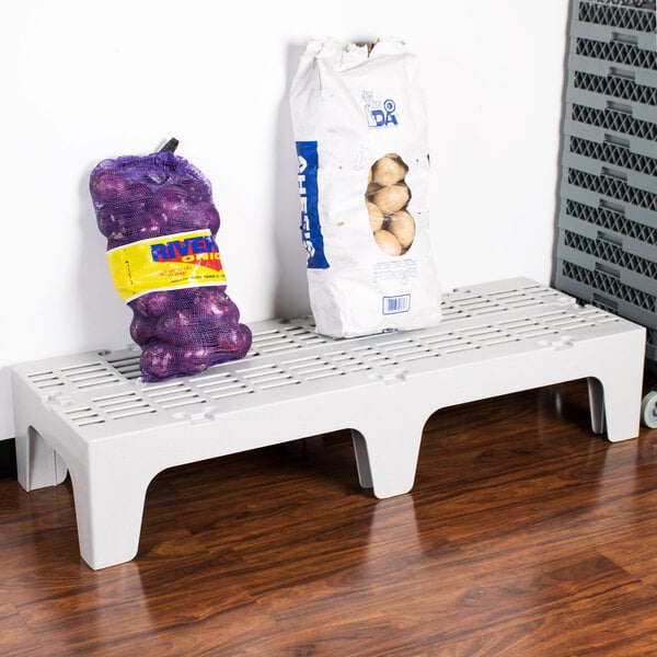 A white Cambro slotted top dunnage rack with a bag of potatoes and a bag of onions on it.