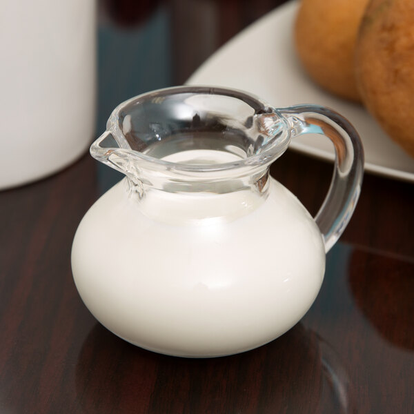 A GET clear plastic creamer filled with milk on a white table.