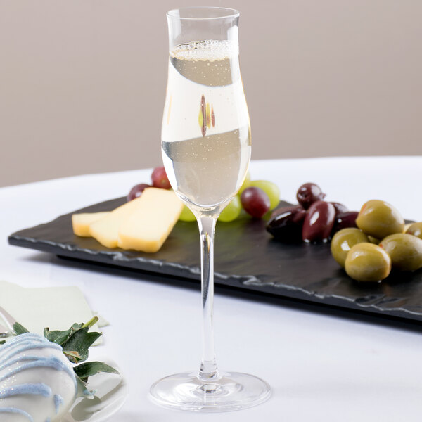 A Stolzle grappa wine glass filled with wine next to a plate of grapes.