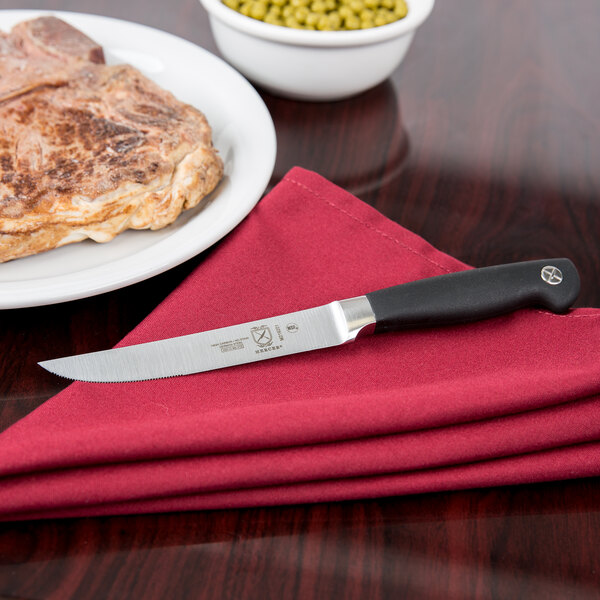 A Mercer Culinary Genesis steak knife on a napkin next to a plate of meat.